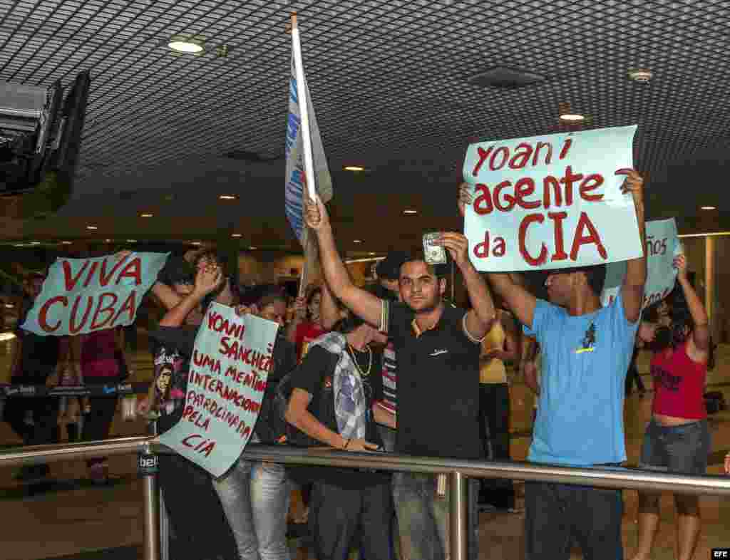 Yoani Sánchez (d), autora del blog "Generación Y" llega hoy, lunes 18 de febrero de 2013, al aeropuerto internacional Guararapes, ciudad de Recife (nordeste de Brasil), en medio de manifestantes que rechazan su visita al país